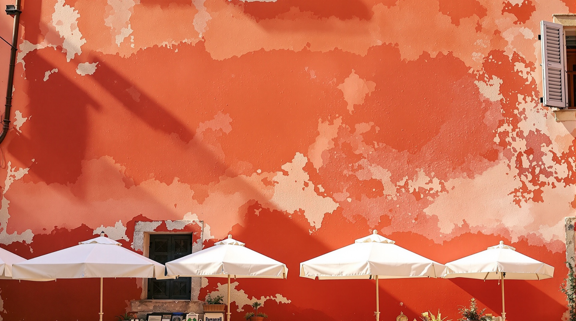 Market umbrellas open against a faded red ochre wall in Italy
